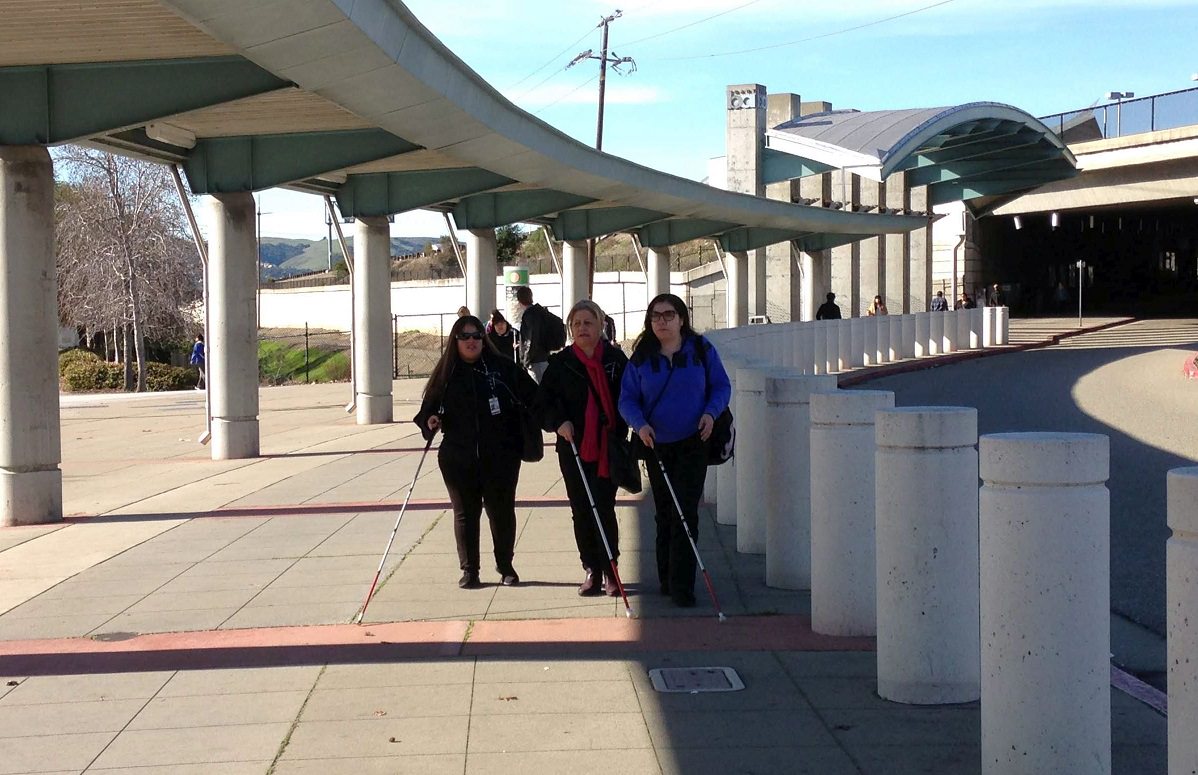 Women who are blind using white canes to travel on a BART platform.